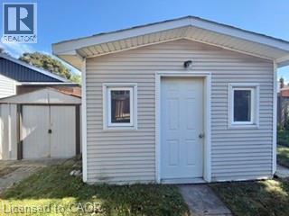 Shed structure featuring horizontal siding, a paneled entry door, and a single-pane window - 499 East 16Th Street, Hamilton, ON