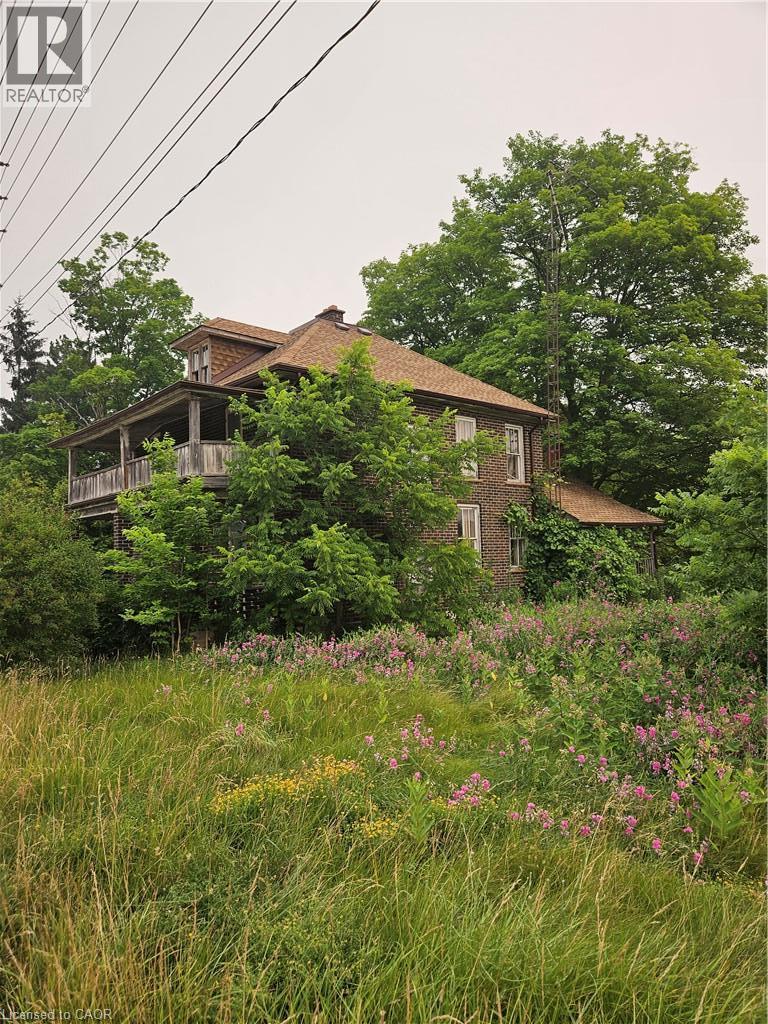 Brick exterior with a multi-level roofline, featuring a wraparound porch with wood railings and structural columns - 1720 Beaverdale Road, Cambridge, ON