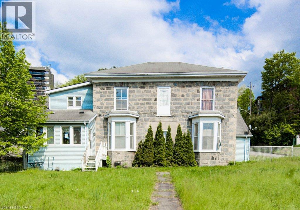 Stone facade residence featuring bay windows, a light blue siding addition, and a sloped roofline - 245 Ainslie Street S, Cambridge, ON