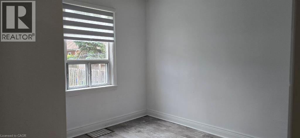 Bright interior space featuring a window with integrated blinds, wood-finish flooring, and white painted walls - 284 Brucedale Avenue E, Hamilton, ON