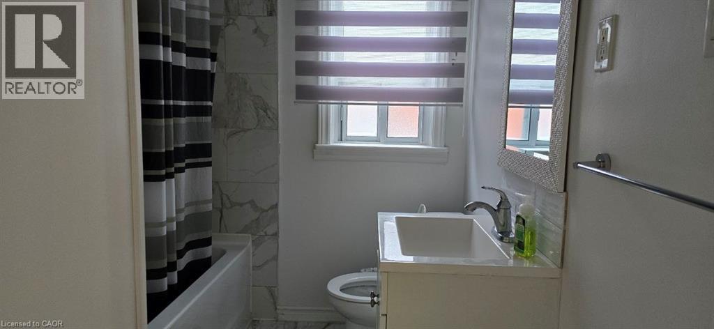 White vanity with integrated sink, chrome faucet, window with privacy blinds, white subway tile backsplash, and full wall tile surround in the shower - 284 Brucedale Avenue E, Hamilton, ON