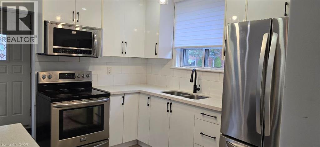 Kitchen featuring white cabinetry with black hardware, stainless steel appliances, a white subway tile backsplash, and light-toned countertops - 284 Brucedale Avenue E, Hamilton, ON