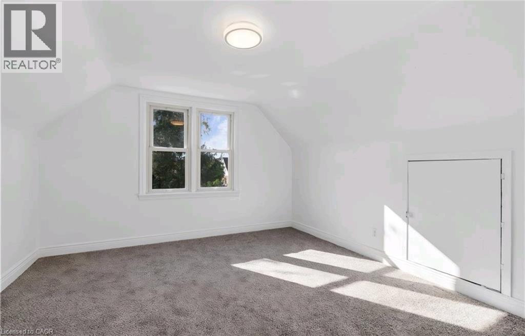 White painted walls, sloped ceiling, gray carpet, double-hung windows, and a flush-mounted ceiling light fixture - 284 Brucedale Avenue E, Hamilton, ON
