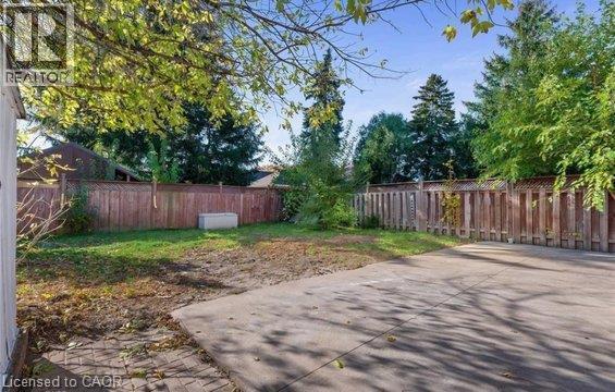 Expansive backyard featuring a concrete patio, brick paver section, wood privacy fencing, and mature trees - 284 Brucedale Avenue E, Hamilton, ON