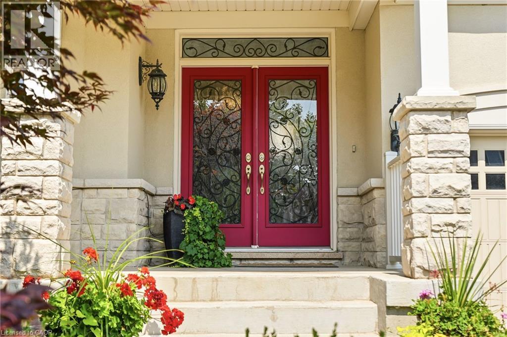 Elegant red double doors with decorative wrought-iron glass panels and transom window, flanked by stone pilasters and complemented by vibrant seasonal plantings and landscape beds - 536 Cusick Circle, Milton, ON