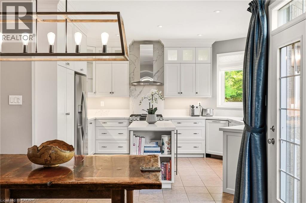 White cabinetry, stainless steel appliances, tiled flooring, wood-finish dining table, and a contemporary chandelier - 536 Cusick Circle, Milton, ON