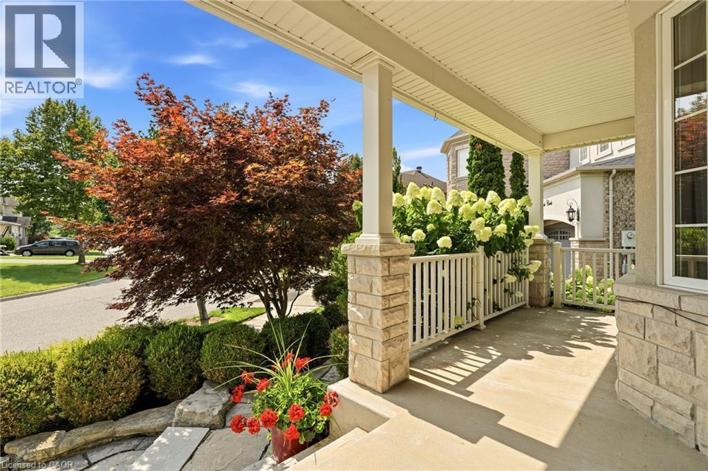 Welcoming front porch with stone columns and white railings, anchored by mature landscaping including a Japanese maple with vibrant fall foliage, manicured hedges, and seasonal plantings in decorative - 536 Cusick Circle, Milton, ON