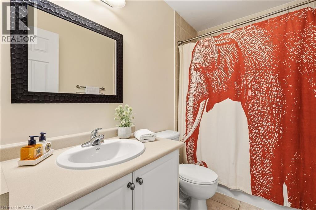 Bathroom featuring a curved white porcelain sink set in a wood-finish vanity with cabinet storage, brushed metal hardware, a large framed mirror with black trim, and a decorative red patterned shower - 536 Cusick Circle, Milton, ON