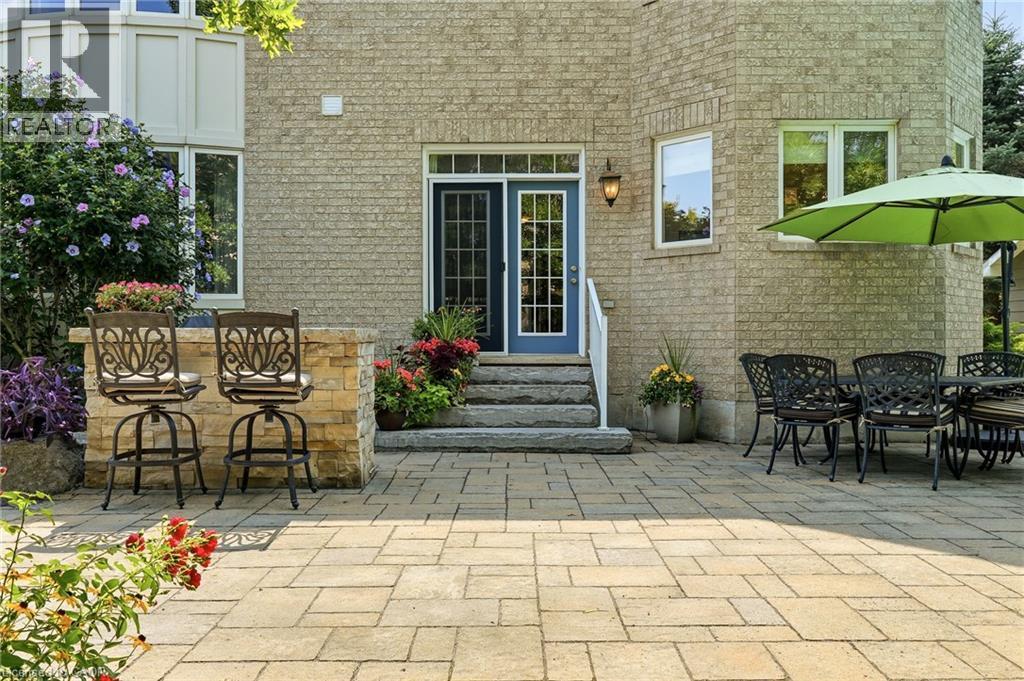 Expansive paver patio with multiple entertaining zones, featuring bistro-height seating, dining furniture arrangement, and mature landscaping with flowering shrubs - 536 Cusick Circle, Milton, ON
