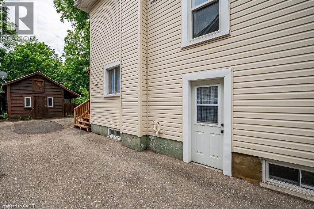 Cream-colored horizontal siding, white trim windows, white door with glass panel, and a wooden accessory building with white-framed windows - 275 Main Street, Cambridge, ON