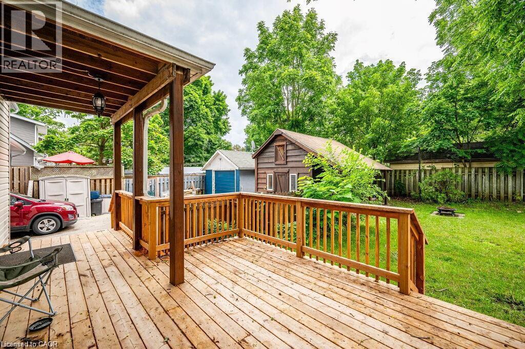 Expansive wooden deck with a covered area and railing, featuring a large grassy yard and a detached shed - 275 Main Street, Cambridge, ON