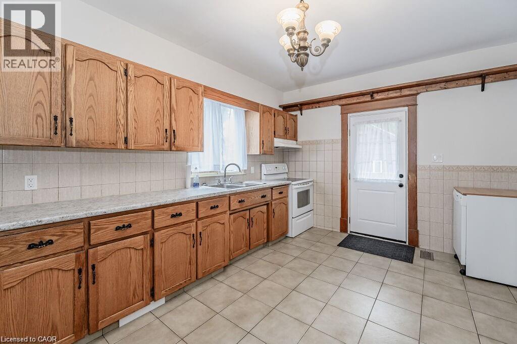 Wood-finish cabinetry with black hardware, light-toned tiled flooring, white tiled backsplash, and a white door with wood trim - 275 Main Street, Cambridge, ON
