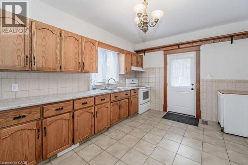 Wood-finish cabinetry with black hardware, light-toned tiled flooring, white tiled backsplash, and a white door with wood trim - 275 Main Street, Cambridge, ON 