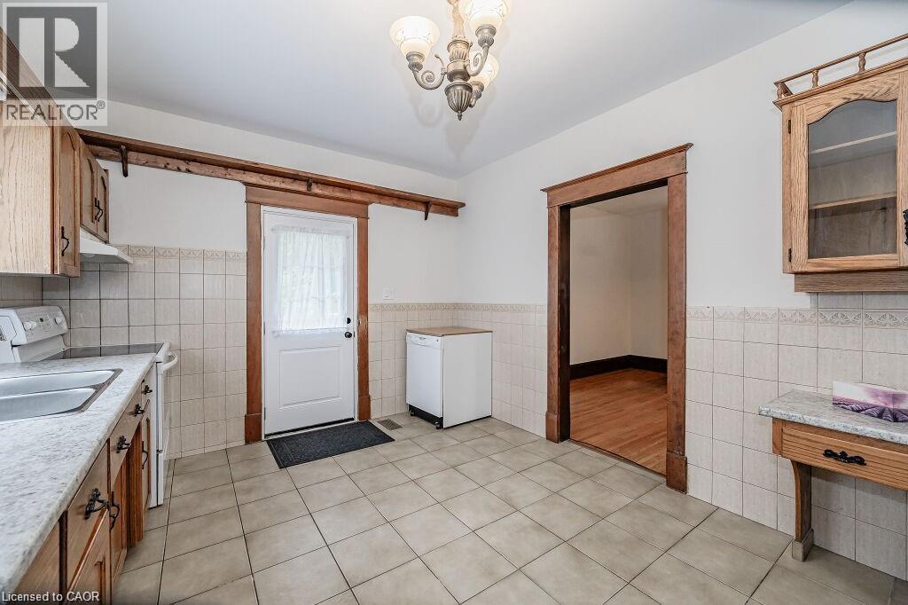 Tile flooring, wood cabinetry, stone-finish countertops, ceramic tile backsplash, and a decorative chandelier - 275 Main Street, Cambridge, ON