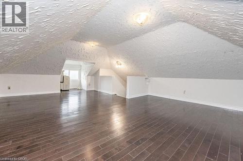 Spacious area featuring wood-finish flooring, white painted walls, and sloped textured ceilings with flush mount lighting - 275 Main Street, Cambridge, ON 