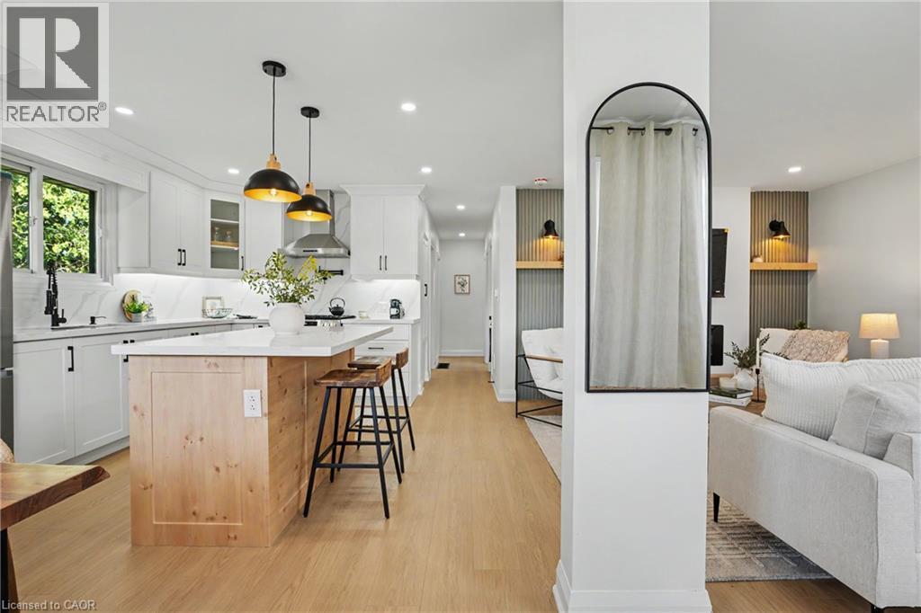 White cabinetry with black hardware, wood-finish flooring, island with wood-finish base, stainless steel range hood, and pendant lighting - 311 East 14Th Street, Hamilton, ON