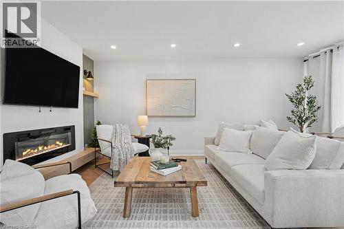 Modern living room featuring a linear gas fireplace with black surround and wood-finish mantel, wall-mounted flat-screen television, recessed ceiling lighting, neutral upholstered seating, wood-finish - 311 East 14Th Street, Hamilton, ON 