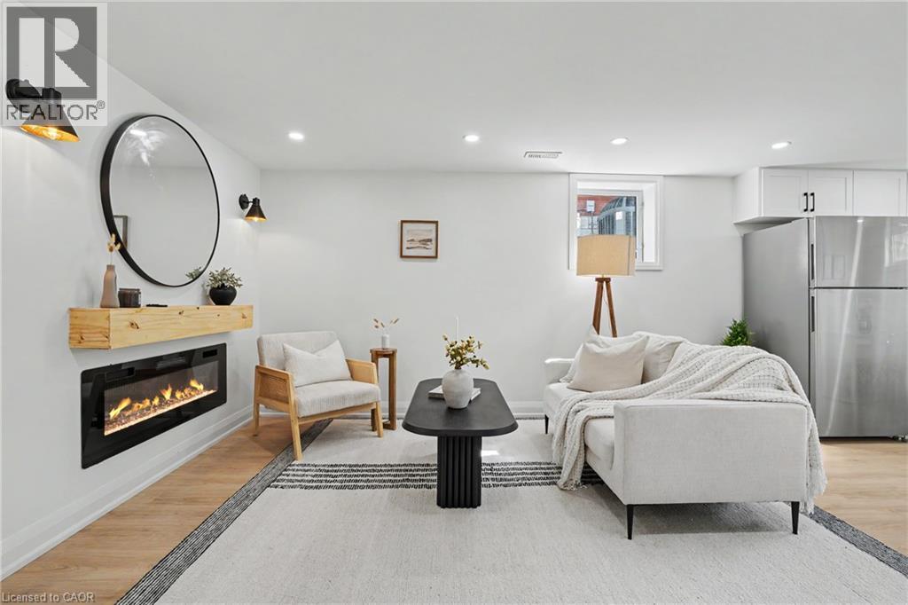 Recessed lighting, wood-finish flooring, electric fireplace with wood mantel, white cabinetry with dark hardware, and a stainless steel refrigerator - 311 East 14Th Street, Hamilton, ON