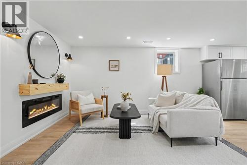 Recessed lighting, wood-finish flooring, electric fireplace with wood mantel, white cabinetry with dark hardware, and a stainless steel refrigerator - 311 East 14Th Street, Hamilton, ON 