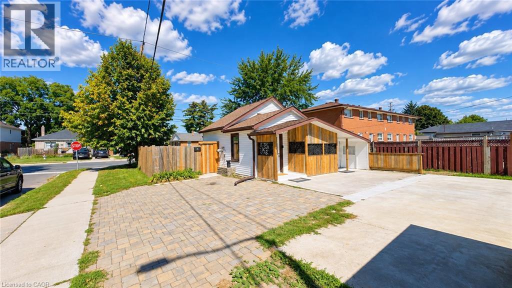 Exterior featuring white siding, wood-paneled accents, a brown shingled roof, a paved driveway, and a wood privacy fence - 76 Avenue Road, Cambridge, ON