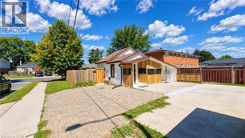 Exterior featuring white siding, wood-paneled accents, a brown shingled roof, a paved driveway, and a wood privacy fence - 76 Avenue Road, Cambridge, ON 