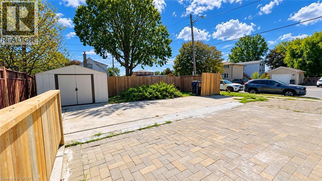 Expansive paved driveway with permeable brick pavers, mature landscaping with established trees, detached storage shed, and wooden privacy fencing throughout the property - 76 Avenue Road, Cambridge, ON
