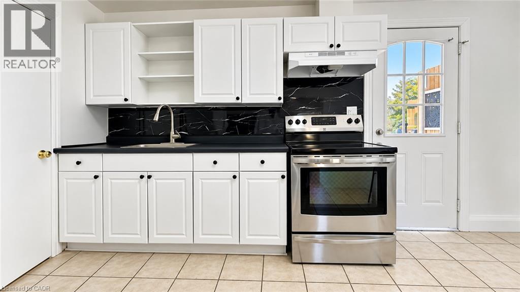 White cabinetry with black hardware, dark countertops, black marble-patterned backsplash, stainless steel range, and a door with arched window panes - 76 Avenue Road, Cambridge, ON
