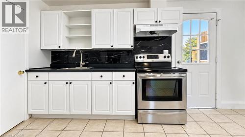 White cabinetry with black hardware, dark countertops, black marble-patterned backsplash, stainless steel range, and a door with arched window panes - 76 Avenue Road, Cambridge, ON 