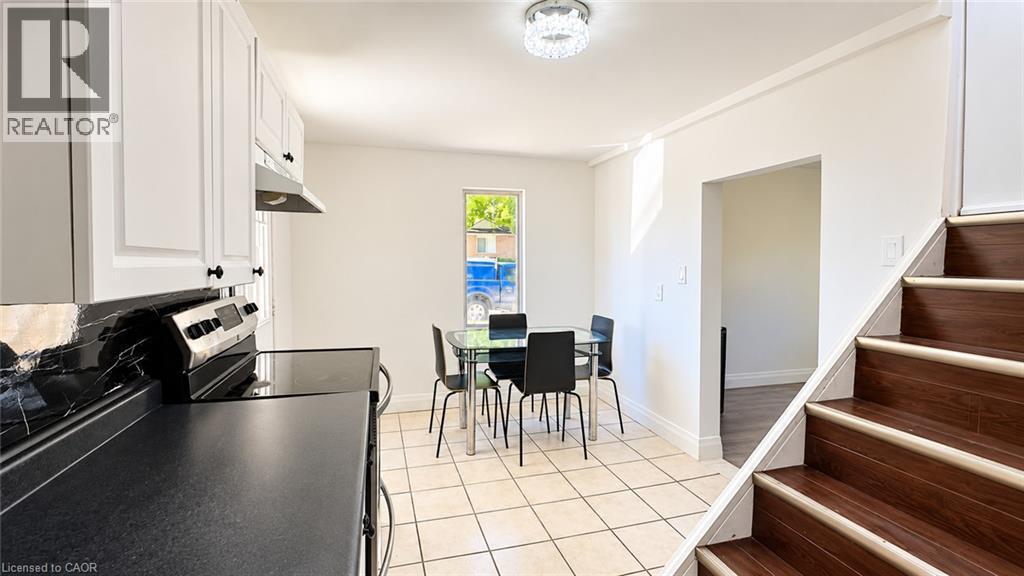 White shaker-style cabinetry with matte black hardware, black countertop, stainless steel range with hood, and ceramic tile flooring - 76 Avenue Road, Cambridge, ON