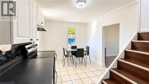 White shaker-style cabinetry with matte black hardware, black countertop, stainless steel range with hood, and ceramic tile flooring - 76 Avenue Road, Cambridge, ON 