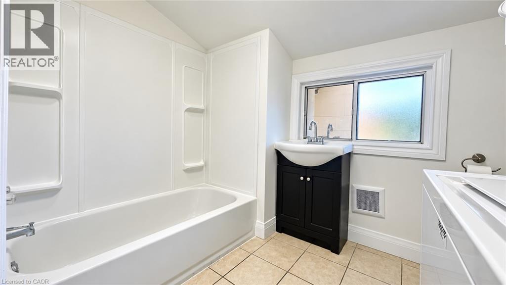 White bathtub with integrated shelving, black vanity with a vessel sink, and a privacy window - 76 Avenue Road, Cambridge, ON