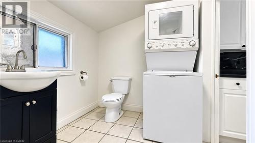 White-tiled flooring, dark-finish vanity with an integrated sink, satin nickel faucet, and a stacked white washer and dryer unit - 76 Avenue Road, Cambridge, ON 