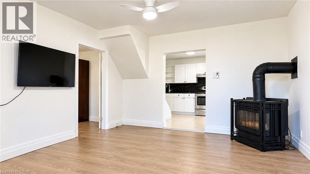 Wood-finish flooring, white walls, ceiling fan, and a black wood-burning stove - 76 Avenue Road, Cambridge, ON