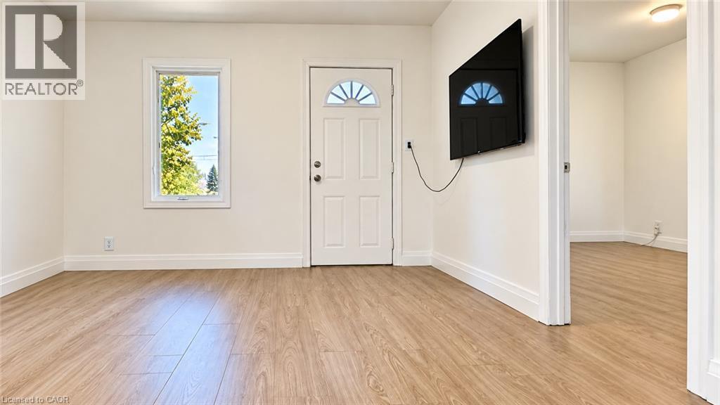 Wood-finish flooring throughout, bright white walls, white trim, and a white entrance door with an arched window insert - 76 Avenue Road, Cambridge, ON
