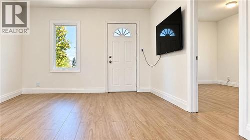 Wood-finish flooring throughout, bright white walls, white trim, and a white entrance door with an arched window insert - 76 Avenue Road, Cambridge, ON 