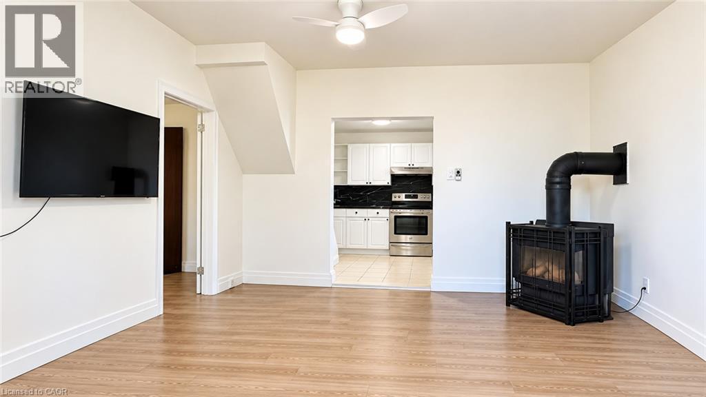Wood-finish flooring throughout, featuring an open-concept layout, a ceiling fan, and a freestanding fireplace - 76 Avenue Road, Cambridge, ON