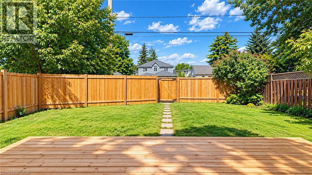 Expansive backyard featuring a wood deck, manicured lawn, full privacy fencing, a stone pathway, and a rear gate - 76 Avenue Road, Cambridge, ON