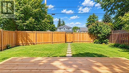 Expansive backyard featuring a wood deck, manicured lawn, full privacy fencing, a stone pathway, and a rear gate - 76 Avenue Road, Cambridge, ON 