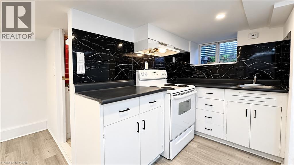 Kitchen featuring white cabinetry, dark countertops, black and white patterned backsplash, and a built-in range - 76 Avenue Road, Cambridge, ON