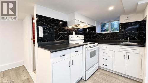 Kitchen featuring white cabinetry, dark countertops, black and white patterned backsplash, and a built-in range - 76 Avenue Road, Cambridge, ON 