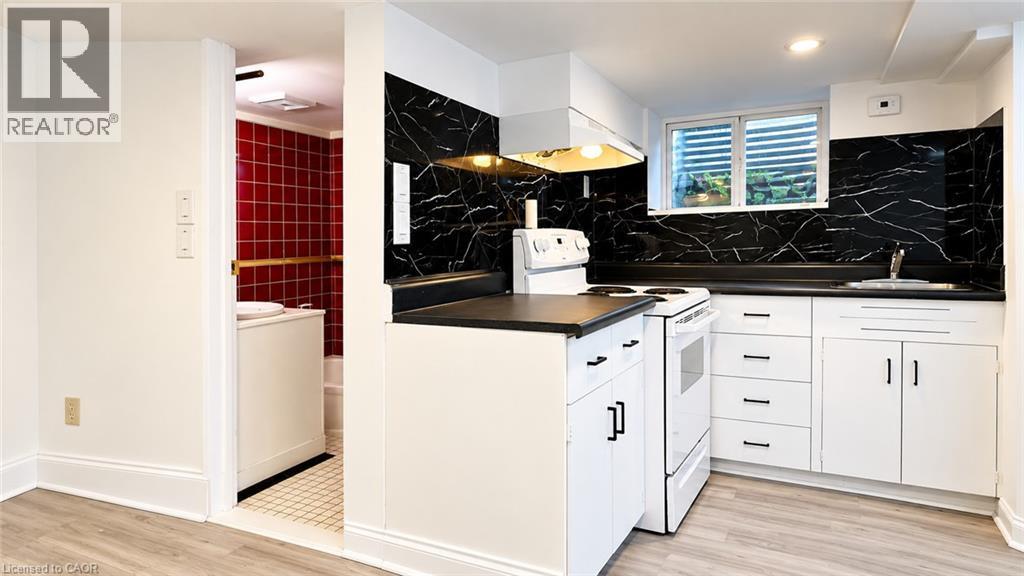 Kitchenette with white cabinetry, black countertops, and a black and white patterned backsplash - 76 Avenue Road, Cambridge, ON