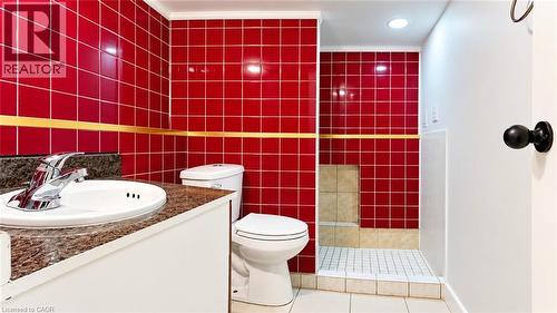 Vanity with stone-finish countertop and chrome faucet, red tiled walls, integrated shower with tiled floor, and recessed lighting - 76 Avenue Road, Cambridge, ON 