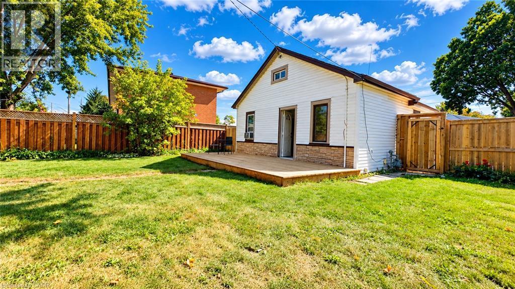 Expansive backyard with a wooden fence, featuring a ground-level deck, white siding, and a rear entry - 76 Avenue Road, Cambridge, ON