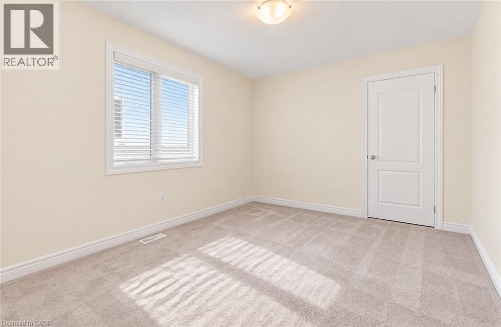Neutral-toned walls and carpeting, featuring a window with blinds, a flush-mount ceiling light, and a white interior door - 61 Duckworth Road, Cambridge, ON
