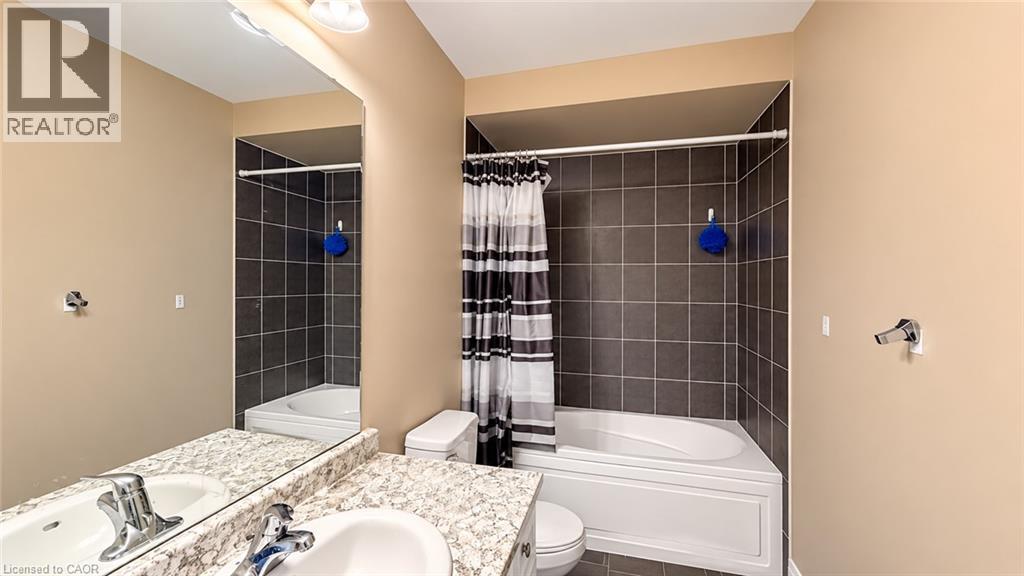 Bathtub with dark tile surround, vanity with dual sinks, speckled countertop, and large wall-mounted mirror - 61 Duckworth Road, Cambridge, ON