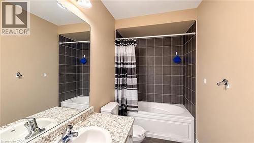 Bathtub with dark tile surround, vanity with dual sinks, speckled countertop, and large wall-mounted mirror - 61 Duckworth Road, Cambridge, ON 