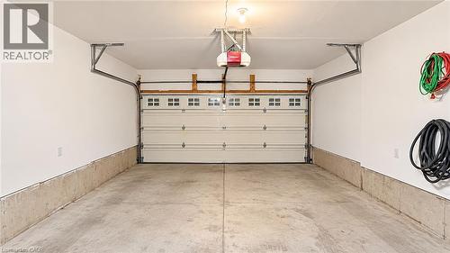 Concrete flooring garage with an automatic overhead door, featuring upper window panels and a wall-mounted garage door opener - 61 Duckworth Road, Cambridge, ON 