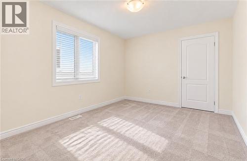 Neutral-toned walls and carpeting, featuring a window with blinds, a flush-mount ceiling light, and a white interior door - 61 Duckworth Road, Cambridge, ON 
