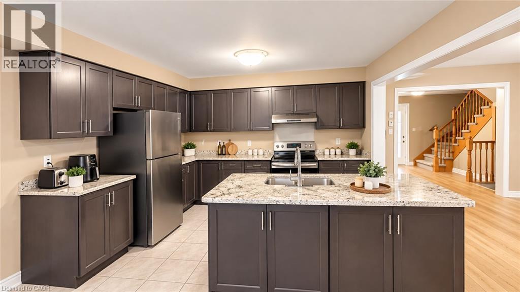 Kitchen featuring dark wood-finish cabinetry, light speckled countertops, stainless steel appliances, and a central island with an undermount sink - 61 Duckworth Road, Cambridge, ON