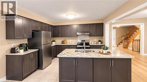 Kitchen featuring dark wood-finish cabinetry, light speckled countertops, stainless steel appliances, and a central island with an undermount sink - 61 Duckworth Road, Cambridge, ON 